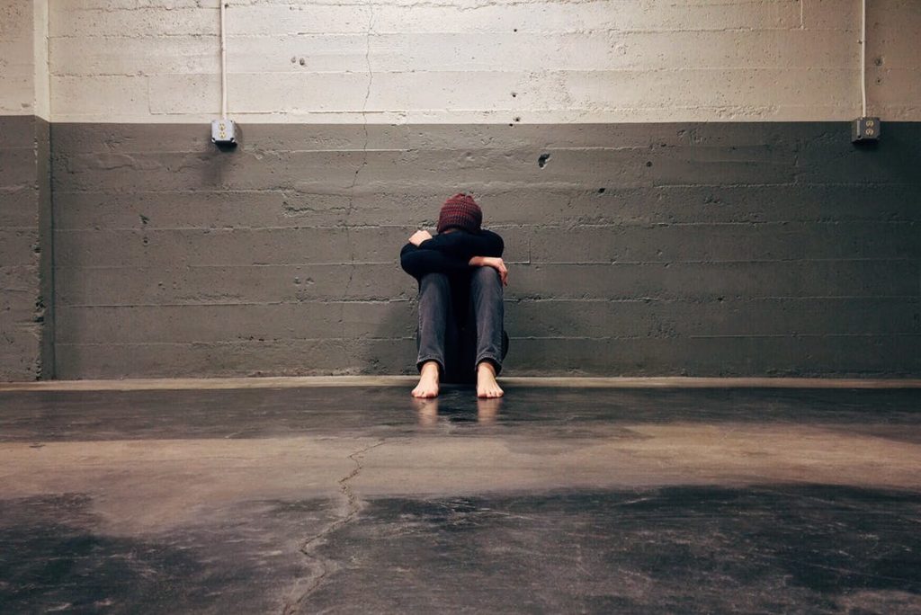 Barefoot teen sitting up against a wall with their head in their arms